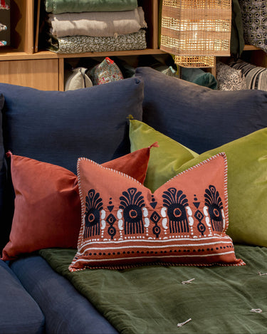 Cojín bordado terracota combinado con textiles de varios colores sobre un sofá azul