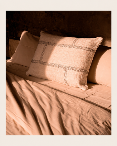 Funda de cojín rectangular de algodón natural de Bazar Bizar, sobre una cama
