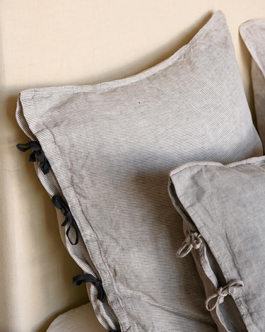 Fundas de almohada Caravane: detalle del lino gris y los lazos negros junto a textiles claros