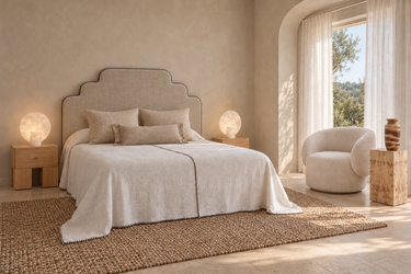Dormitorio de hotel boutique con cabecero de lino a medida con ribete, lámparas de alabastro, mesitas de roble, textiles naturales, sillón de bouclé y jarrón vintage de Matuta Home.
