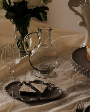 Jarra Nelly de cristal transparente con pie en una mesa vestida, vista de ambiente de Olsson & Jensen