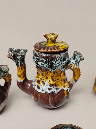 Cafetera de cerámica moteada con remates animales y tapa.