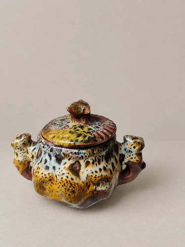 Azucarero moteado con tapa y pequeñas asas figurativas.