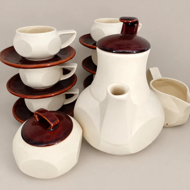 Cafetera, lechera, azucarero y tazas apiladas del juego blanco y marrón.