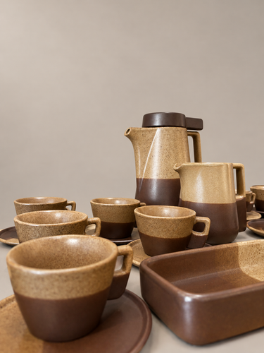 Juego de café vintage de gres beige y marrón: detalle de cafetera, lechera, tazas y bandeja sobre fondo topo claro