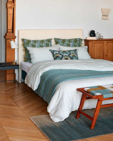 Cama vestida en tonos claros y verdes con banco de madera a los pies