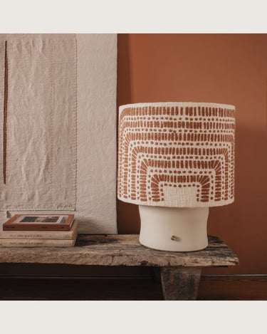 Lámpara de mesa de cerámica con pantalla de arcos cálidos de âme philo, sobre un banco junto a libros