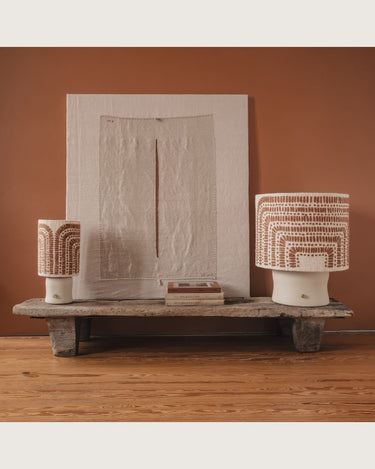 Lámpara de mesa de cerámica con pantalla de arcos cálidos, dos lámparas sobre un banco con un cuadro textil