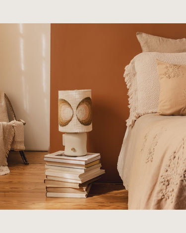 Lámpara de mesa de cerámica con pantalla de círculos multicolor de âme philo, sobre una pila de libros junto a la cama