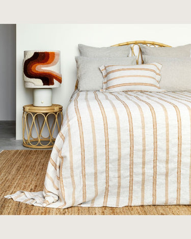Lámpara de mesa de cerámica con pantalla en tonos tierra y rojos, junto a una cama con textiles a rayas