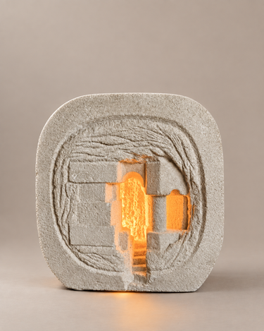 Lámpara de piedra vintage encendida, con luz ámbar en los huecos del relieve arquitectónico