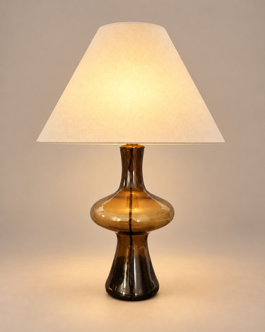 Lámpara de mesa vintage de vidrio ahumado ámbar con pantalla crema, encendida sobre fondo topo claro
