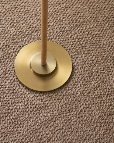 Detalle de la base circular dorada sobre una alfombra de fibra natural.