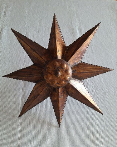 Lámpara solar vintage dorada vista de frente, con ocho rayos triangulares y centro circular abombado