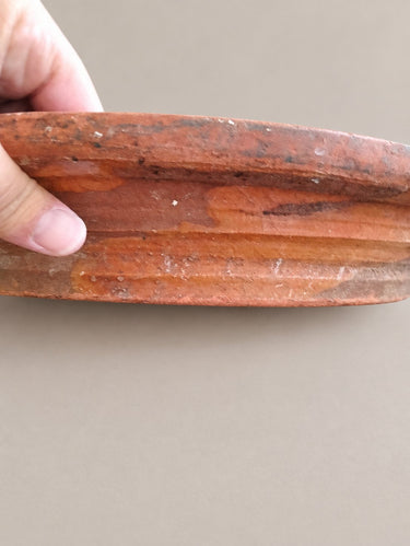 Detalle lateral del borde del lebrillo, sostenido por una mano, con manchas y marcas de uso