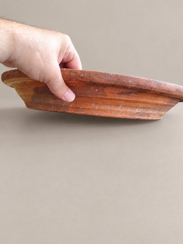 Perfil lateral del lebrillo de barro sostenido por una mano, sobre fondo topo claro