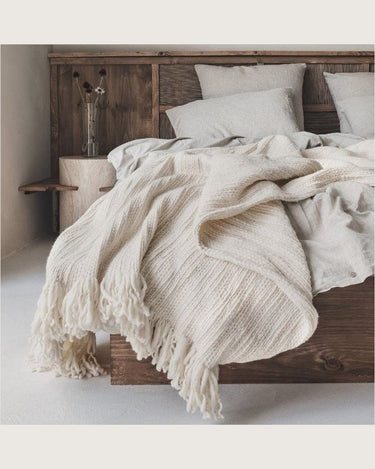 Manta de lana gruesa blanco crudo de Bed and Philosophy, sobre una cama con cabecero de madera