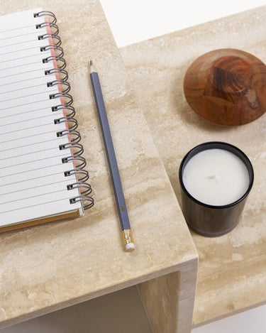 Cuaderno y lápiz sobre el plano alto, con vela y objeto de madera debajo.