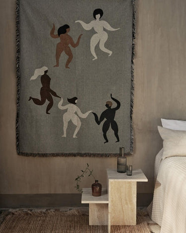 Mesa de Ferm Living: mesa junto a una cama con jarra, vaso y pequeño jarrón.