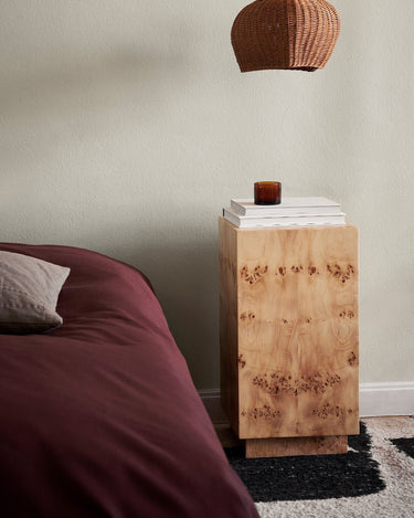 Mesa junto a cama de tonos rojizos, con libros y vela encima.