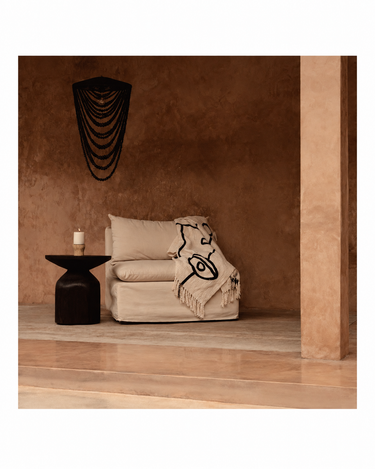 Mesa auxiliar redonda de madera oscura, vista de conjunto junto a una butaca blanca