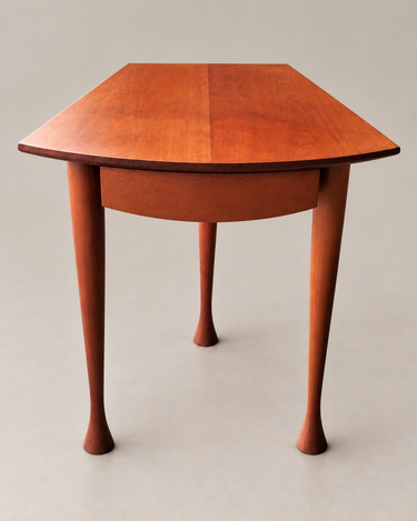 Mesa auxiliar vintage de madera con el tablero curvo y las patas completas sobre fondo topo claro