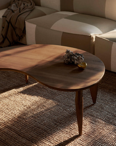 Composición de salón con mesa de nogal, objeto pétreo y sofá claro.