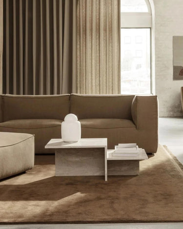 Mesa de Ferm Living: mesa de centro frente a sofá beige, con jarrón blanco y libros.
