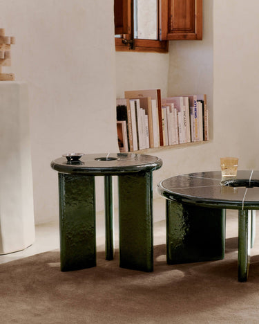 Dos mesas verdes Deya junto a una pared revocada, con libros y recipientes sobre los tableros.