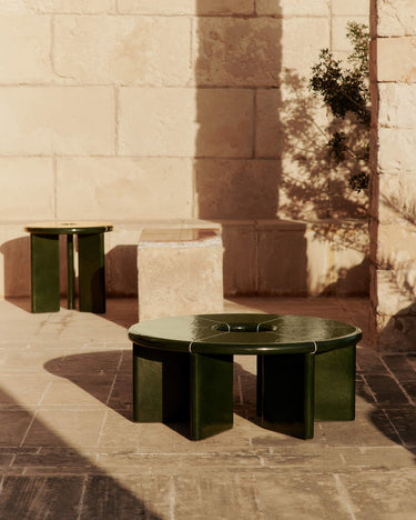 Mesa de Ferm Living: mesa baja redonda y mesa auxiliar alta de la misma serie sobre terraza de piedra.