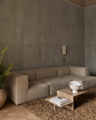 Mesa de Ferm Living: mesa de centro junto a sofá beige con cerámica blanca y libros.