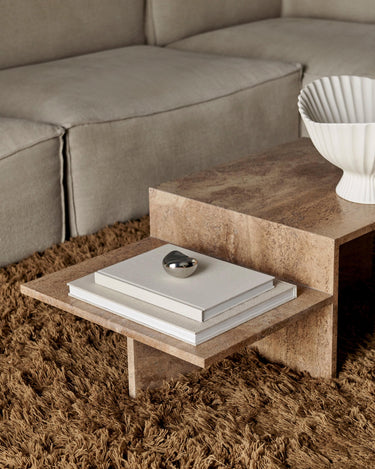 Mesa sobre alfombra de pelo con libros, cuenco metálico y cerámica.