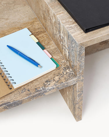Planos de travertino con cuaderno azul, bolígrafo y carpeta negra.