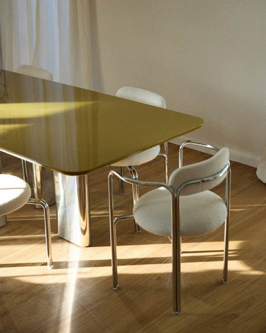 Mesa de comedor lacada con patas de acero inoxidable de Gabrielle Paris, tablero verde oliva junto a sillas claras
