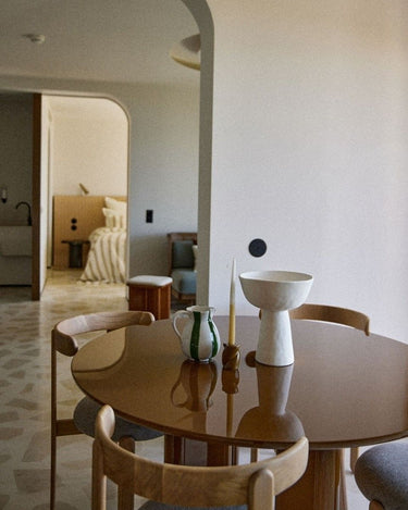 Mesa de comedor lacada caramelo con un cuenco blanco y sillas de madera