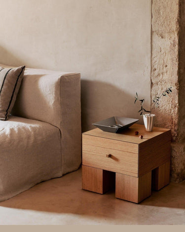 Una de las mesitas Kuben junto a un sofá beige, con un objeto rectangular oscuro sobre la superficie.