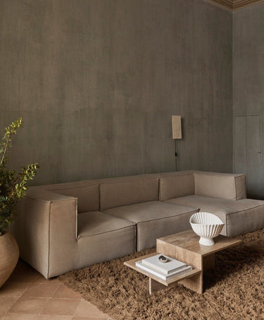 Módulo central profundo de sofá de lino natural de Ferm Living: ambiente con composición de varios módulos claros, mesa pétrea y pared gris.