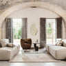 Módulo profundo de lino con extremo abierto derecho de Ferm Living: sala bajo arco de piedra con sofás modulares claros enfrentados y sillón marrón al fondo; encuadre vertical de ambiente.