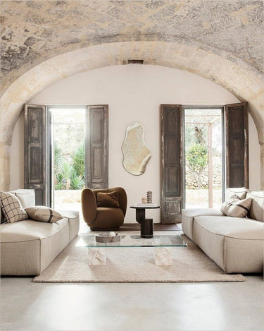 Módulo profundo de lino con extremo abierto derecho de Ferm Living: sala bajo arco de piedra con sofás modulares claros enfrentados y sillón marrón al fondo; encuadre vertical de ambiente.