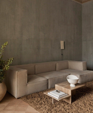 Módulo de sofá profundo de lino con brazo derecho de Ferm Living: ambiente de composición modular clara con mesa pétrea, jarrón blanco y pared gris; varios módulos juntos.