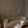 Módulo de sofá profundo de lino con brazo izquierdo de Ferm Living: ambiente de sofá modular de varios asientos frente a pared gris, mesa baja pétrea y jarrón blanco.