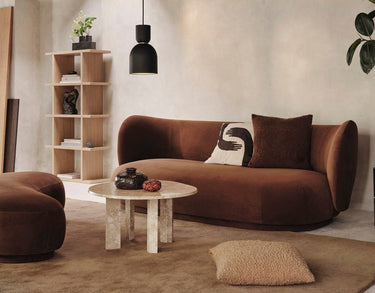 Otomana de Ferm Living: ambiente de sofá marrón y otomana parcial a la izquierda, mesa baja clara y estantería; bandas lisas superior e inferior.