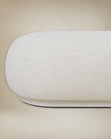 Otomana de Ferm Living: detalle del extremo redondeado y zócalo de la otomana blanco roto, textura del tejido.