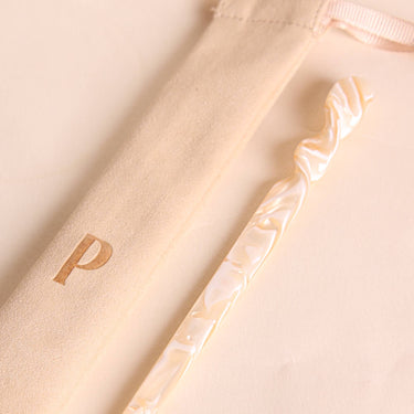 Palillo para el pelo de acetato crema y caramelo de Peignée Paris, junto a su bolsa de presentación.