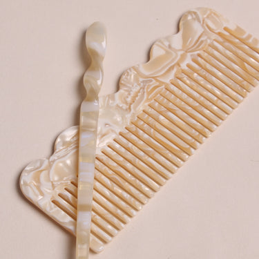 Palillo para el pelo de acetato crema y caramelo de Peignée Paris, junto a un peine del mismo acabado.