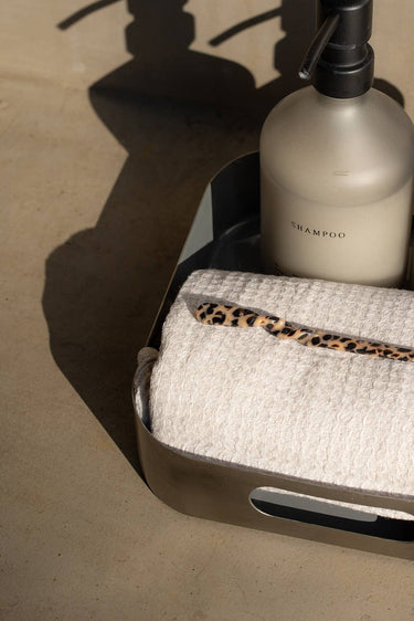 Palillo para el pelo de acetato con estampado de leopardo de Peignée Paris, en una escena de baño con toalla.