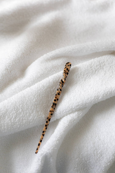 Palillos para el pelo de acetato con estampado de leopardo de Peignée Paris: una pieza sobre una toalla blanca.