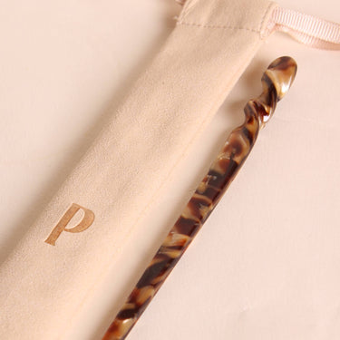 Palillo para el pelo de acetato marrón efecto carey de Peignée Paris, junto a su bolsa de presentación.