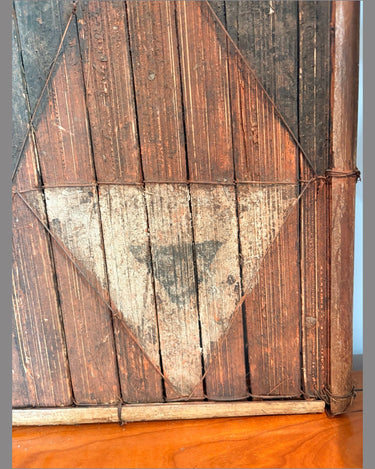 Detalle original del panel salampasu: triángulo negro sobre fondo crema, lamas verticales y ataduras del marco