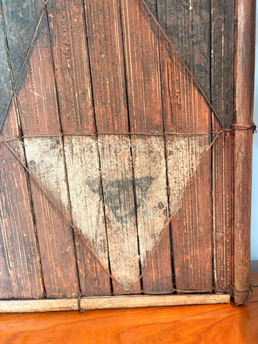 Detalle original del panel salampasu: triángulo negro sobre fondo crema, lamas verticales y ataduras del marco